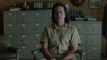 Movie still from “Twin Peaks” (2017), directed by David Lynch – A man sitting in a chair in front of filing cabinets; Medium shot, Low angle