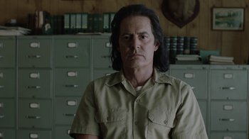Movie still from “Twin Peaks” (2017), directed by David Lynch – A man with long black hair is standing in front of some filing cabinets; Medium shot, Over the shoulder angle