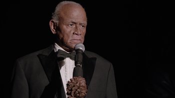 Movie still from “Twin Peaks” (2017), directed by David Lynch – An older man in a tuxedo holding a microphone; Close Up shot, Over the shoulder angle