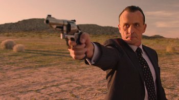 Movie still from “Twin Peaks” (2017), directed by David Lynch – A man in a suit and tie pointing a gun; Medium shot, Low angle