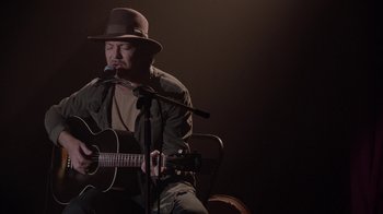 Movie still from “Twin Peaks” (2017), directed by David Lynch – A man with a hat is playing a guitar; Medium shot, High angle
