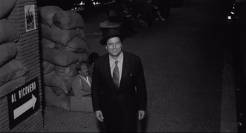 Movie still from “Two Women” (1960), directed by Vittorio De Sica – A black and white photo of a man in a suit and hat; Wide shot, High angle