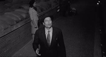 Movie still from “Two Women” (1960), directed by Vittorio De Sica – A man wearing a suit and hat walking down a street; Medium shot, Low angle