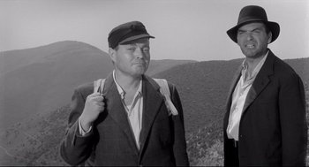 Movie still from “Two Women” (1960), directed by Vittorio De Sica – A man wearing a hat and a jacket standing next to another man wearing a hat; Medium shot, Low angle