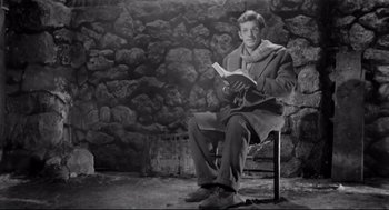 Movie still from “Two Women” (1960), directed by Vittorio De Sica – A man sitting on a chair reading a book; Medium shot, Low angle