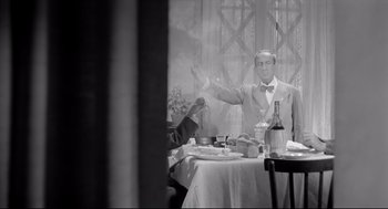 Movie still from “Two Women” (1960), directed by Vittorio De Sica – A man sitting at a dinner table with his arms outstretched; Medium shot, Low angle