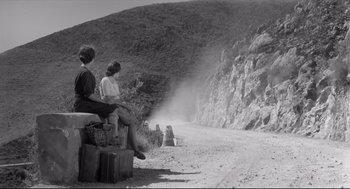 Movie still from “Two Women” (1960), directed by Vittorio De Sica – Two people sitting on a bench on a dirt road; Wide shot, Low angle