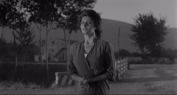 Movie still from “Two Women” (1960), directed by Vittorio De Sica – A black and white photo of a woman standing in front of a fence; Medium shot, Low angle