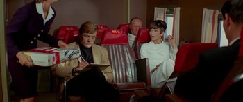 Movie still from “Two for the Road” (1967), directed by Stanley Donen – A man and a woman sitting on a red airplane seat; Medium shot, High angle