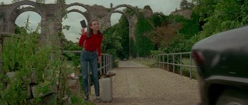 Movie still from “Two for the Road” (1967), directed by Stanley Donen – A young woman holding a cell phone while standing on a bridge; Medium shot, Low angle