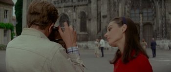 Movie still from “Two for the Road” (1967), directed by Stanley Donen – A man taking a picture of a woman in front of a building; Close Up shot, Over the shoulder angle