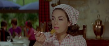 Movie still from “Two for the Road” (1967), directed by Stanley Donen – A woman in a pink and white checkered shirt eating noodles; Close Up shot, Over the shoulder angle