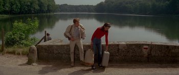 Movie still from “Two for the Road” (1967), directed by Stanley Donen – A man and a woman holding suitcases next to a body of water; Wide shot, High angle