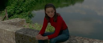 Movie still from “Two for the Road” (1967), directed by Stanley Donen – A woman sitting on a rock near a body of water; Medium shot, High angle