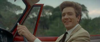 Movie still from “Two for the Road” (1967), directed by Stanley Donen – A man in a suit sitting in the driver's seat of a red car; Close Up shot, Over the shoulder angle