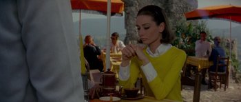 Movie still from “Two for the Road” (1967), directed by Stanley Donen – A woman sitting at an outdoor table in front of a tea pot; Medium shot, Over the shoulder angle