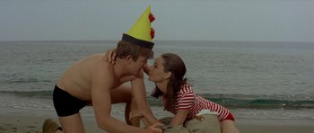 Movie still from “Two for the Road” (1967), directed by Stanley Donen – A man and a woman wearing a party hat on the beach; Medium shot, High angle