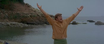 Movie still from “Two for the Road” (1967), directed by Stanley Donen – A man standing in the water with his arms outstretched; Medium shot, Low angle
