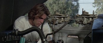 Movie still from “Two-Lane Blacktop” (1971), directed by Monte Hellman – A man working on an engine of a train car; Close Up shot, Low angle