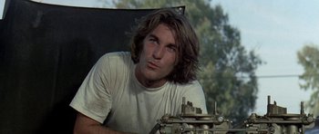 Movie still from “Two-Lane Blacktop” (1971), directed by Monte Hellman – A man sitting in a chair looking at the camera; Close Up shot, Low angle