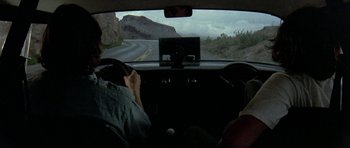 Movie still from “Two-Lane Blacktop” (1971), directed by Monte Hellman – A man driving a car on the side of the road; Wide shot, High angle