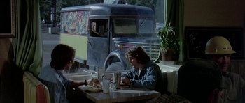 Movie still from “Two-Lane Blacktop” (1971), directed by Monte Hellman – Two people sitting at a table in front of a truck; Wide shot, Over the shoulder angle