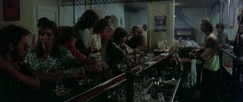 Movie still from “Two-Lane Blacktop” (1971), directed by Monte Hellman – A group of people sitting at a bar drinking wine; Wide shot, Over the shoulder angle