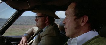 Movie still from “Two-Lane Blacktop” (1971), directed by Monte Hellman – Two men are sitting in the back seat of a car; Close Up shot, Over the shoulder angle