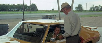 Movie still from “Two-Lane Blacktop” (1971), directed by Monte Hellman – A man in a yellow car with a man in a brown hat; Medium shot, Over the shoulder angle