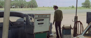Movie still from “Two-Lane Blacktop” (1971), directed by Monte Hellman – A man standing in front of a gas pump; Wide shot, Over the shoulder angle