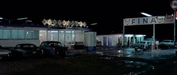 Movie still from “Two-Lane Blacktop” (1971), directed by Monte Hellman – An empty parking lot at night with cars parked in front of it; Extreme Wide shot, Low angle