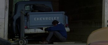 Movie still from “Two-Lane Blacktop” (1971), directed by Monte Hellman – A man sitting on the back of a blue chevrolet truck; Wide shot, High angle