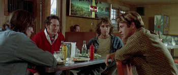 Movie still from “Two-Lane Blacktop” (1971), directed by Monte Hellman – A group of people sitting at a table in a restaurant; Medium shot, Over the shoulder angle