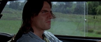 Movie still from “Two-Lane Blacktop” (1971), directed by Monte Hellman – A man sitting in the driver's seat of a car looking out the window; Close Up shot, Low angle