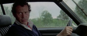 Movie still from “Two-Lane Blacktop” (1971), directed by Monte Hellman – A man sitting in the drivers seat of a car in the rain; Close Up shot, Low angle
