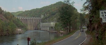 Movie still from “Two-Lane Blacktop” (1971), directed by Monte Hellman – A view of a lake with a large dam in the background; Extreme Wide shot, High angle