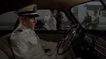 Movie still from “U-571” (2000), directed by Jonathan Mostow – A man in a uniform sitting in the driver's seat of a car; Medium shot, High angle