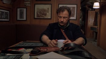 Movie still from “U-571” (2000), directed by Jonathan Mostow – A man sitting at a table with a cup of coffee; Medium shot, High angle