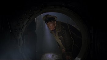 Movie still from “U-571” (2000), directed by Jonathan Mostow – A man wearing a hat and a jacket is looking through a hole in the wall; Medium shot, Low angle