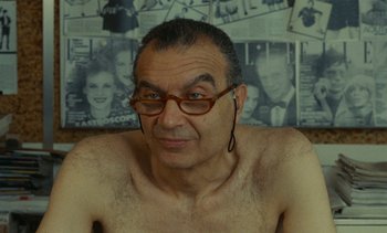 Movie still from “Ulysse” (1983), directed by Agnès Varda – A man with glasses and a beard is posing for a picture; Close Up shot, Over the shoulder angle