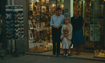 Movie still from “Ulysse” (1983), directed by Agnès Varda – A man and two women and a child standing in front of a store; Wide shot, High angle