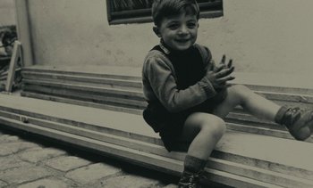 Movie still from “Ulysse” (1983), directed by Agnès Varda – A little boy sitting on some steps and clapping; Medium shot, High angle