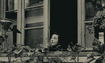 Movie still from “Ulysse” (1983), directed by Agnès Varda – A woman looking out of a window with plants in front of it; Close Up shot, Low angle