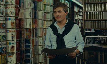 Movie still from “Ulysse” (1983), directed by Agnès Varda – A man in a book store holding a book; Medium shot, Over the shoulder angle