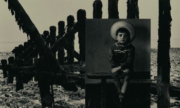 Movie still from “Ulysse” (1983), directed by Agnès Varda – A young boy sitting on a bench in front of wooden posts; Medium shot, Low angle