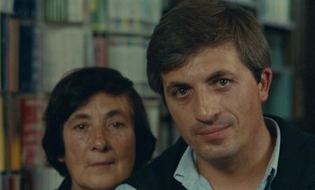 Movie still from “Ulysse” (1983), directed by Agnès Varda – A man and a woman standing next to each other in a library; Close Up shot, Over the shoulder angle