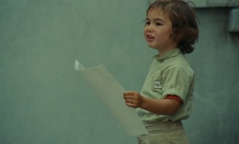 Movie still from “Ulysse” (1983), directed by Agnès Varda – A little girl holding a piece of paper in front of a green wall; Close Up shot, High angle