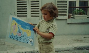 Movie still from “Ulysse” (1983), directed by Agnès Varda – A little boy is holding a painting on the sidewalk; Medium shot, High angle