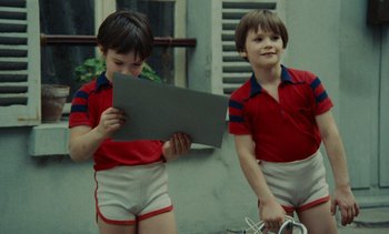 Movie still from “Ulysse” (1983), directed by Agnès Varda – Two young boys in red shirts and white shorts holding a piece of paper; Medium shot, Low angle