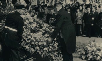 Movie still from “Ulysse” (1983), directed by Agnès Varda – An old black and white photo of a man laying a wreath; Medium shot, High angle